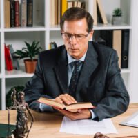 mature-male-lawyer-reading-book-with-gavel-justice-statue-wooden-table